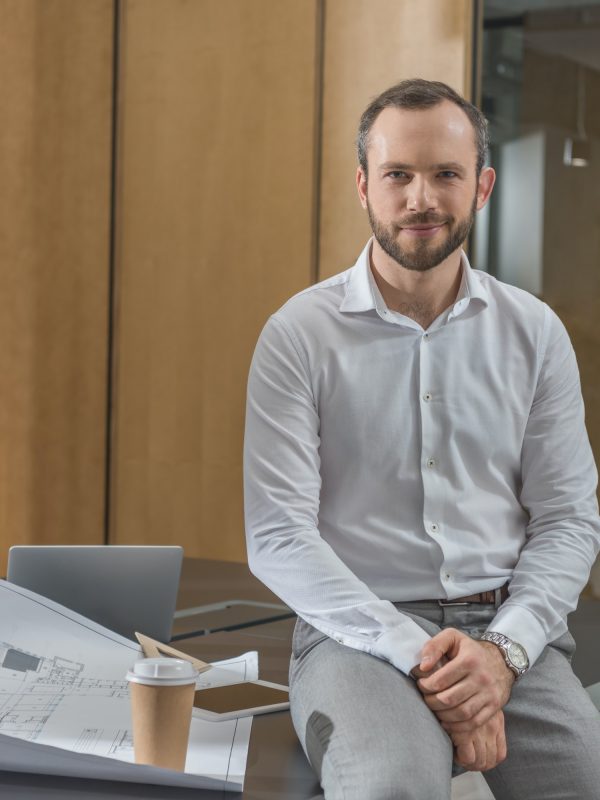 handsome-architect-sitting-on-table-with-plans-at-office.jpg